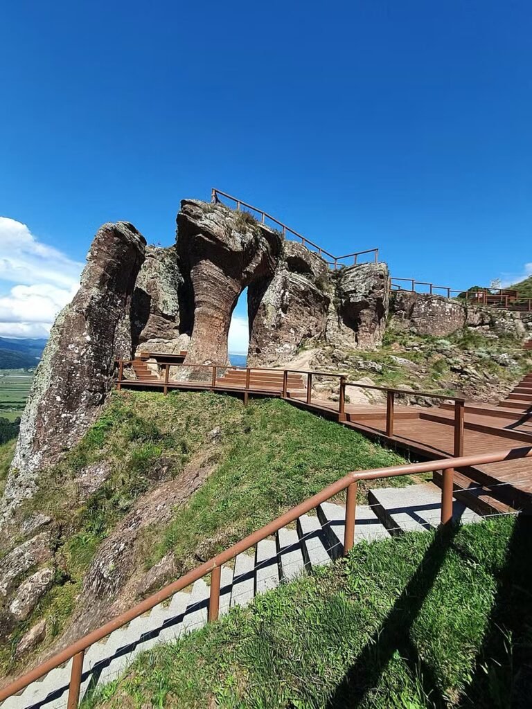 O arco de arenito do Morro do Campestre, com passarela de madeira e o vale ao fundo. Foto do Parque Morro do Campestre